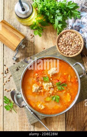 Tomatenlinsensuppe mit Fleischbällchen und Gemüse auf einem Holztisch. Draufsicht flach lagen Hintergrund. Stockfoto