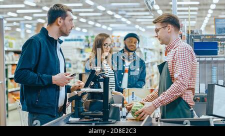 Im Supermarkt: Kasse Counter Kunde zahlt mit Smartphone für seine Artikel. Großes Einkaufszentrum mit freundlicher Kasse, kleinen Linien und modern Stockfoto