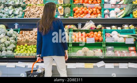 Im Supermarkt: Frau wählt Bio-Früchte in der Frischwarenabteilung des Stores. Sie sucht Cantaloupe. Warenkorb Wird Gehalten Stockfoto