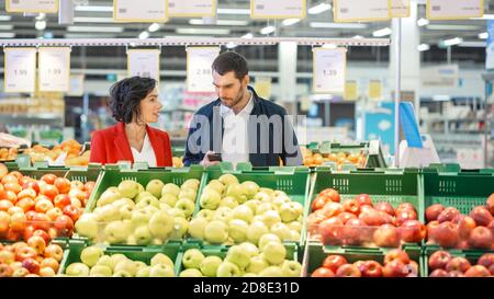 Im Supermarkt: Das glückliche junge Paar wählt Bio-Gemüse in der Frischwarenabteilung des Stores. Freund und Freundin abholen Stockfoto