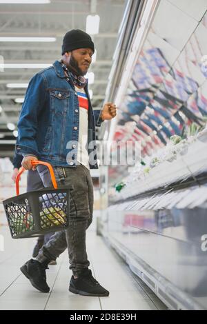 Im Supermarkt: Ganzlängenaufnahme eines stylischen African American Guy tanzt durch die Fresh Produce Section des Stores. Viel Spaß Beim Einkaufen Stockfoto
