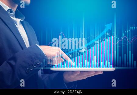Mann in Anzug hält Tablet mit futuristischen Hologramm Grafik und Arbeitet am Wachstumsdiagramm Stockfoto