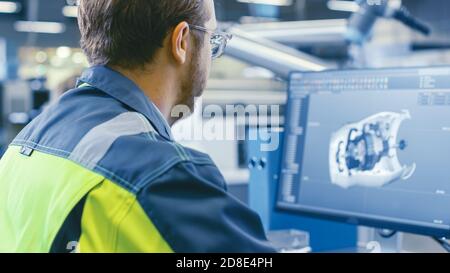 Zurück Aufnahme eines Maschinenbauingenieurs, der an Computern arbeitet, Entwicklung im 3D-Modell des Motors mit CAD-Software. In der Fabrik. Stockfoto