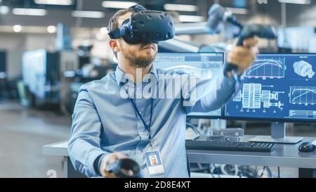 Portraitaufnahme des Industrietechnikers mit Virtual Reality-Headset und Verwendung von Controllern, bereit zur Arbeit. Im Hintergrund Fertigungswerk Stockfoto