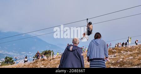 Jalta, Russland - 20. September 2020: Schönes, kühnes Mädchen mit langen weißen Haaren, die auf dem Trolley auf dem Kabel auf dem hohen Bergplatt herumlaufen Stockfoto