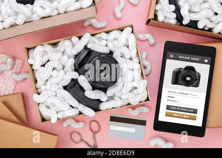 Online-Shopping von Digitalkamera und andere elektronische Produkte Konzept. Tablet-Computer mit Online-Shop-App auf dem Bildschirm umgeben von Paketen mit Pro Stockfoto