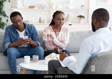 Sucht Nach Smartphones. Verärgerte Afrikanische Frau Beschwert Sich Über Gleichgültigen Ehemann Zu Familienrat Stockfoto