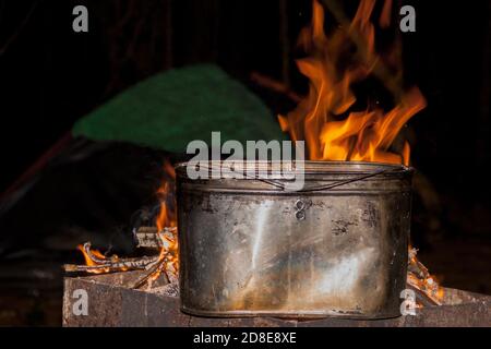 Abendessen auf dem Campingplatz. Kessel auf einem brennenden Feuer, Feuer, Rauch. Kochen auf einer Reise. Wilde Ruhe. Stockfoto