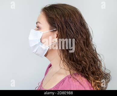 Junge Frau in medizinischen Gesichtsschutz Maske auf blauem Hintergrund, Seitenansicht. Stockfoto
