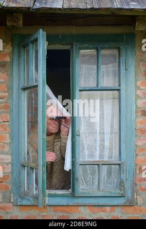 Miserable suchen älter männlich Vorhang twitcher Spionage auf Nachbarn aus Fenster, um jemanden zu finden, der die Regeln für die Sperrung einer Coronavirus-Pandemie bricht Stockfoto