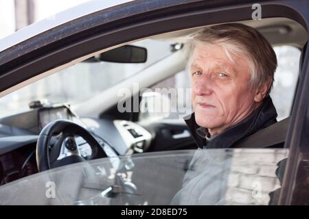 Älterer kaukasischer Mann ein Fahrer, der mit strenger Optik im Auto sitzt, hat ein Seitenfenster geöffnet Stockfoto