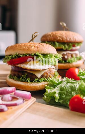 Zwei hausgemachte frische, leckere Burger mit Salat und Käse. Zutaten auf dem Tisch. Heller Hintergrund für Speisen. Stockfoto