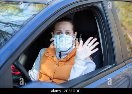 Portrait einer Fahrerin, die Auf Wiedersehen oder Hallo zu seinem Beifahrer sagt, kaukasische Frau, die eine One Use Maske trägt Stockfoto