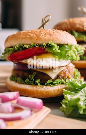 Zwei hausgemachte frische, leckere Burger mit Salat und Käse. Zutaten auf dem Tisch. Heller Hintergrund für Speisen. Stockfoto