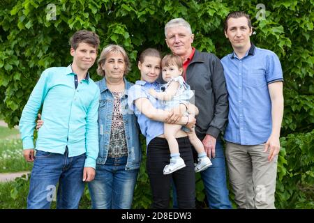 Sechs Personen kaukasisches Familienportrait gegen einen grünen Baum, ältere Großeltern, Erwachsene alleinerziehender Vater, Mädchen und Jungen im Jugendalter, Kleinkind Stockfoto
