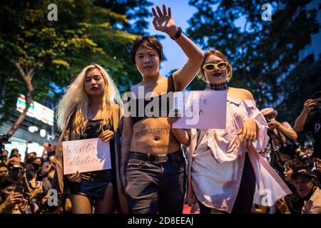 Eine prodemokratische Protesterin mit einem Crop Top (C) geht mit zwei Protestierenden auf der Landebahn während einer Modenschau bei einer Anti-Regierung-Demonstration in der thailändischen Hauptstadt. Tausende von prodemokratischen Demonstranten gingen in Silom auf die Straße und forderten den Rücktritt des thailändischen Premierministers und die Reform der Monarchie. Das Thema des heutigen Protestes war "People's Runway", ein Mock Fashion "roter Teppich", der mit der Modenschau zusammenfällt, die von Thailands Prinzessin Sirivannavari am selben Tag für ihre brandneue Kollektion organisiert wurde. Der Protest endete friedlich mit den Demonstranten Danci Stockfoto