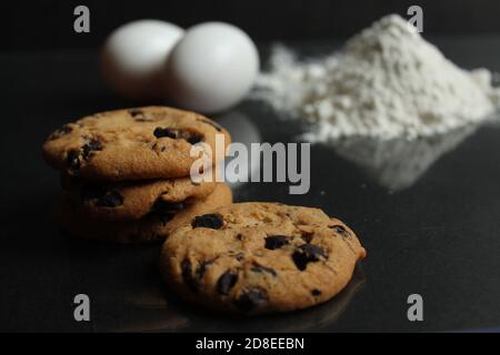 Küche Stillleben Kochprozess hausgemachte Schokoladenkekse mit Schokolade Tropfen im Hintergrund Mehl und Hühnereier liegen auf Ein schwarzer Spiegel zurück Stockfoto