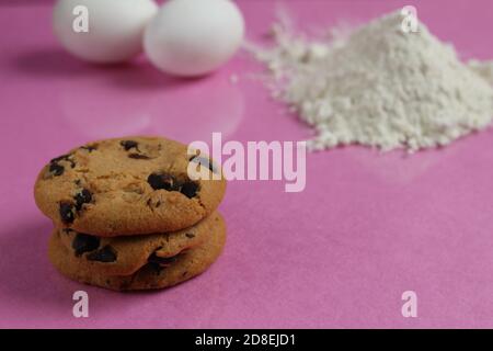 Küche Kochprozess hausgemachte Schokoladenkekse mit Schokolade Tropfen in Der Hintergrund Mehl und Hühnereier liegen auf einem rosa Fuchsia Spiegel hinten Stockfoto