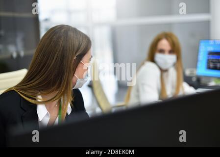 Zwei weibliche Mitarbeiter Büroleiter in Gesichtsmasken reden an Arbeitsplatz im modernen Büro Stockfoto