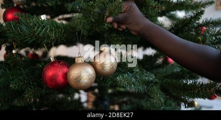 Hand eines Kindes hängend glänzend goldenen Urlaub Kugel auf weihnachtsbaum. Stockfoto
