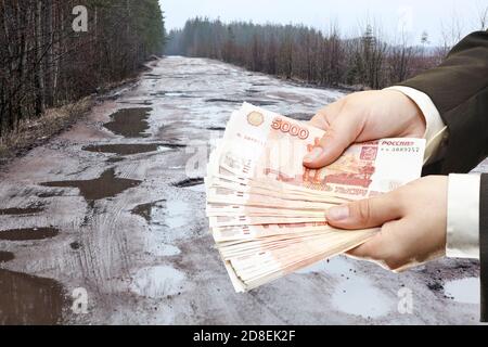 Menschliche Hände halten russische Rubel vor dem Hintergrund von alten Asphaltstraße voller Schlaglöcher, Collage Stockfoto