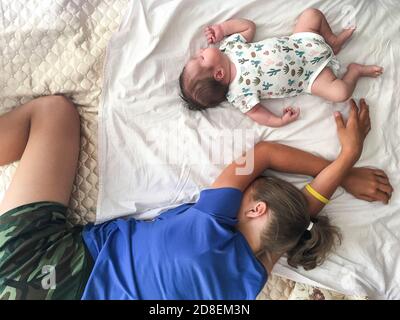 Zwei kaukasische Schwestern ein neugeborenes Baby und Teenager-Mädchen schlafen zusammen im Bett, Draufsicht Stockfoto