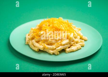 Makkaroni mit Cheddar auf einem Teller minimal auf einem grünen Hintergrund. Köstliche hausgemachte Mahlzeit, mac und Käse. Stockfoto