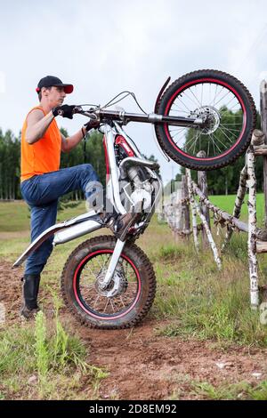 Fellow mit Test Mototrycle Training im ländlichen Raum, Anheben Fahrrad auf Hinterrad, lehnte sich gegen ländlichen Zaun Stockfoto