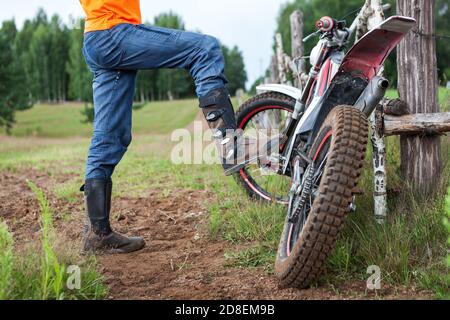 Mann Fahrer steht in der Nähe Schmutz Motorrad in der Landschaft, Schritte mit Boot auf Fahrrad Haken Stockfoto
