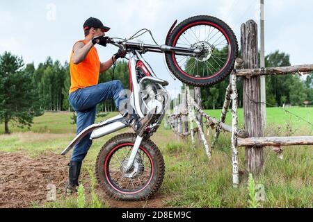 Mann Fahrer mit Test Mototrycle Training im ländlichen Bereich, Anheben Fahrrad auf Hinterrad, lehnte sich gegen Holzzaun Stockfoto