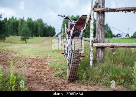 Freizeit Off-Road-Motorrad lehnt an ländlichen Holzzaun im Dorf, Rückansicht, Copyspace Stockfoto