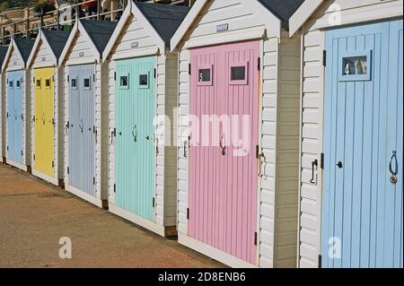 Lyme Regis, Dorset und weiche, pastellfarbene Holztüren zieren Strandhütten an der Strandpromenade. Stockfoto