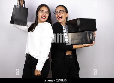 Zwei junge schöne Frauen halten schwarze Einkaufstaschen und Boxen lächelnd zueinander. Schwarzer Freitag Stockfoto