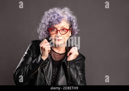 Porträt der schönen alten Frau trägt Lederjacke auf einem Grauer Hintergrund Stockfoto