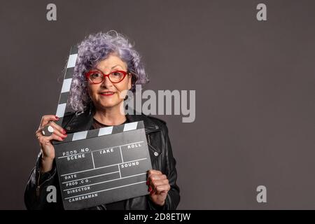 Porträt der schönen alten Frau hält einen Film Klapper auf Ein grauer Hintergrund Stockfoto