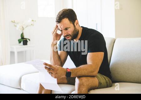 Depressive reifen Mann hält Papier und Blick auf sie, während Sitzen auf der Couch zu Hause Stockfoto