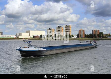 Frachtschiff entlang der Nieuwe Maas in der Nähe des Flusshafens von Rotterdam, gegen einige Wohngebäude und suggestive Himmel. Stockfoto