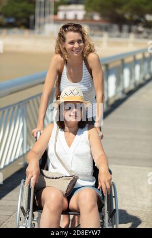 lady schiebt weibliche Freundin im Rollstuhl während im Sommerurlaub Stockfoto