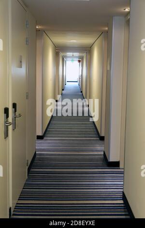 Langer Hotelkorridor mit Türen. Teppiche auf dem Boden, Sonnenlicht am Ende im Hintergrund. Stockfoto