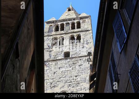 Blick von einer engen Straße im historischen Zentrum von Genua auf den gotischen Glockenturm der Kirche San Giovanni di Pre vor einem blauen klaren Himmel. Stockfoto