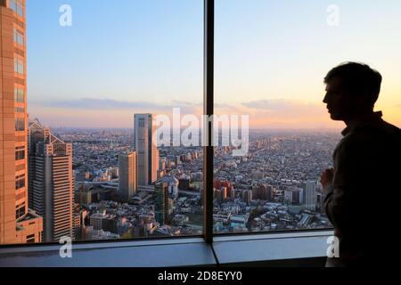 Ein Besucher, der das Stadtbild von Tokyo während des Sonnenuntergangs von betrachtet Die Aussichtsplattform des Tokyo Metropolitan Government Building in Shinjuku.Tokyo.Japan Stockfoto