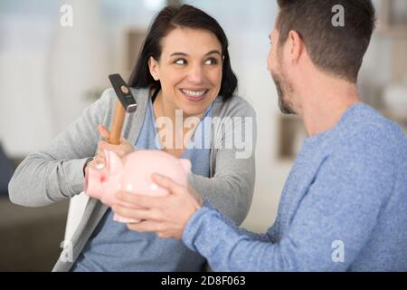 Junges Paar bricht Sparschwein mit Hammer zu Hause Stockfoto