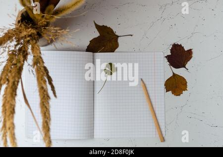 Notizbuch mit einem Lesezeichen aus vierblättrigen Kleeblatt auf dem Hintergrund eines Herbststraußes und Blättern Selektiver Fokus. Stockfoto