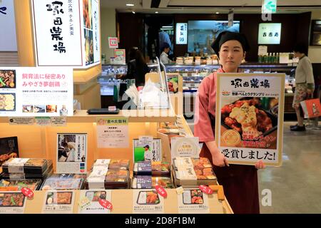 Eine junge Frau, die für einen Imbissstand arbeitet und einen hält Werbetafel für eine preisgekrönte Bento-Mahlzeit.Tokyu Food Show.Tokyu Kaufhaus.Shibuya.Tokyo.Japan Stockfoto