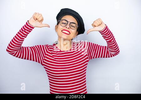 Junge schöne Brünette Frau trägt französisch Baskenmütze und Brille auf weißem Hintergrund zuversichtlich mit Lächeln auf Gesicht, sich mit fing zeigen Stockfoto