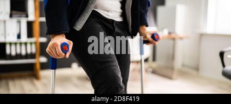 Behinderter Mann, Der Mit Krücken Am Büroarbeitsplatz Steht Stockfoto