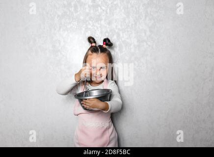 Offen isoliertes Porträt eines ernsthaften 5-jährigen Mädchens in einer großen Schüssel, die Mehl, Eier und Milch aufpeitscht und Pfannkuchen auf eigene Faust zubereitet. Rezept, Kochen Stockfoto