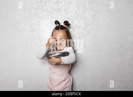 Offen isoliertes Porträt eines ernsthaften 5-jährigen Mädchens in einer großen Schüssel, die Mehl, Eier und Milch aufpeitscht und Pfannkuchen auf eigene Faust zubereitet. Rezept, Kochen Stockfoto