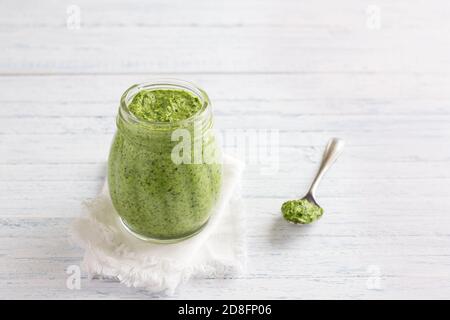 Frische hausgemachte Pesto-Sauce aus Rucola mit Pinienkernen in einem Glas auf blauem Holzhintergrund. Leckere gesunde Lebensmittel. Selektiver Fokus Stockfoto