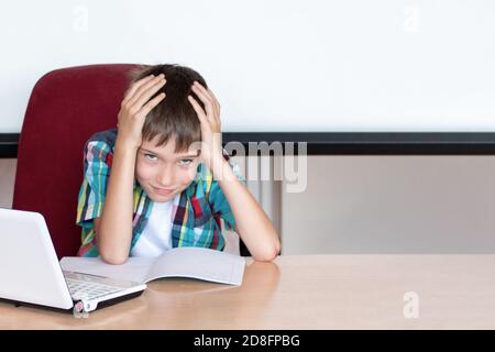 Müder Junge, der seinen Kopf hält, um Hausaufgaben zu machen. Kind mit Lernschwierigkeiten. Ein Junge, der Probleme mit seinen Hausaufgaben hat Stockfoto